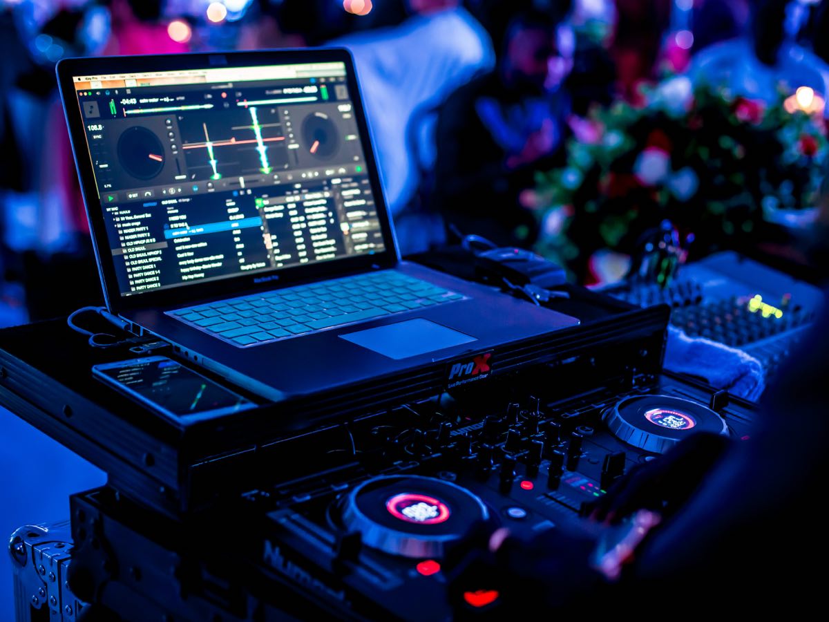 DJ-Controller und Laptop am DJ-Pult, im Hintergrund Blumenschmuck einer Feier