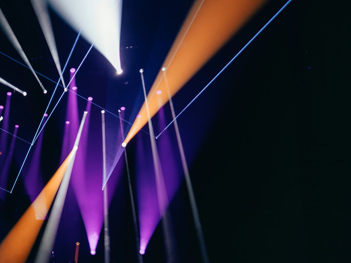Moving Heads auf einer Bühne mit weißen, violetten und orangen Lichtstrahlen